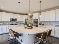 Modern kitchen featuring a large island with quartz countertop, stylish pendant lighting, and stainless steel appliances at 11096 Endeavor Dr, Parker, CO 80134