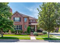 Beautiful brick home with mature trees, landscaped yard, and inviting front porch at 693 Syracuse St, Denver, CO 80230