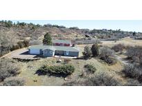 Ranch-style home with a two-car garage on a hillside lot with mature trees and additional red barn-style building at 2485 5Th St, Castle Rock, CO 80104