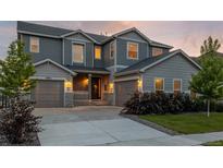 Inviting gray two-story home boasts a three-car garage, manicured landscaping, and a welcoming front porch at 12953 Bridge View Ln, Parker, CO 80134