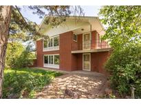 Charming red brick home featuring a unique balcony and mature landscaping at 7475 W Vassar Ave, Lakewood, CO 80227