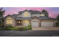 Charming two-story home with a brick facade, gray roof, lush landscaping, and a three-car garage at 6335 Oberon Rd, Arvada, CO 80004