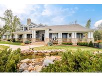 An elegant home showcasing a landscaped yard, a picturesque pond, and an inviting covered porch with stone accents at 5425 S University Blvd, Greenwood Village, CO 80121