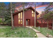 Charming red home with a well-maintained lawn and inviting walkway, surrounded by mature trees, and a colorful sunset at 23646 Genesee Village Rd, Golden, CO 80401