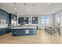 Bright, open kitchen featuring blue cabinetry, a large island with pendant lighting, and stainless steel appliances at 14341 Beebalm Loop, Parker, CO 80134