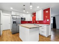 Modern kitchen features stainless steel appliances, white cabinets, butcher block island, and a bold red tiled backsplash at 6948 W 70Th Ave, Arvada, CO 80003