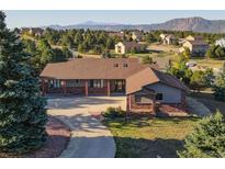 Aerial view of a ranch-style home with mature landscaping, a long driveway, and mountain views at 20120 Doewood Dr, Monument, CO 80132