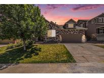 Charming home with a stone facade, well-manicured lawn, mature tree, and driveway leading to a two-car garage at 21444 E Lehigh Ave, Aurora, CO 80013