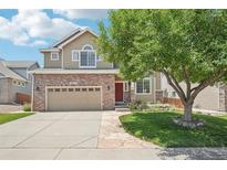 Charming two-story home featuring a red brick facade, manicured lawn, and mature shade tree at 10115 Cook St, Thornton, CO 80229