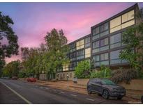 Modern apartment building with large windows and mature trees creating an inviting street view at 1050 N Corona St # 105, Denver, CO 80218