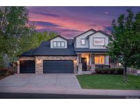 Charming two-story home with a manicured lawn, stone accents, and a spacious three-car garage at dusk at 6488 Tilbury Ave, Firestone, CO 80504