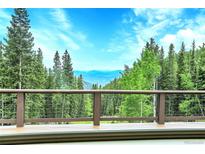 Breathtaking mountain views from a deck with brown railing, surrounded by lush green trees against a stunning blue sky at 1176 Raven Ridge Rd, Idaho Springs, CO 80452