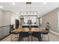 Open-concept dining area with a large wood table and modern lighting, flowing into a kitchen with island at 17233 W 93Rd Pl, Arvada, CO 80007