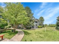 Inviting condo exterior with stone accents, a manicured lawn, mature trees, and blue sky at 8065 W Eastman Pl # 6-102, Denver, CO 80227