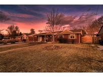 Charming brick ranch-style home with mature tree and well-maintained lawn under a dramatic, colorful sky at 748 S Grape St, Denver, CO 80246