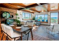 Bright living area featuring wood beam ceiling, tile floors, and large windows offering picturesque mountain views at 21868 Mountsfield Dr, Golden, CO 80401