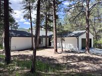 Charming single-story home with light colored exterior paint, dark roof, and surrounded by pine trees at 14546 Pine View Rd, Larkspur, CO 80118