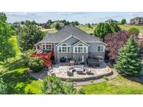 Expansive backyard featuring a stone patio with outdoor seating, hot tub, grill, and a charming raised deck at 9576 E 147Th Pl, Brighton, CO 80602