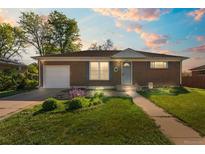 Charming brick home with a well-manicured lawn and an attached one car garage under a colorful sunset at 11320 Irma Dr, Northglenn, CO 80233