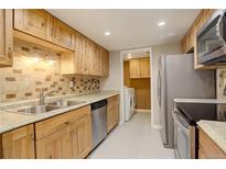 Well-lit kitchen with stainless steel appliances, tile backsplash, and light wood cabinets at 3550 S Harlan St # 259, Denver, CO 80235