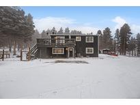 Two-story home with a deck and snowy yard surrounded by pine trees at 26788 Richmond Hill Rd, Conifer, CO 80433