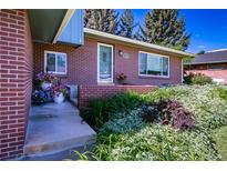 Charming brick home featuring a colorful garden and inviting front entrance with a covered porch and flower-filled planters at 5404 W Rowland Pl, Littleton, CO 80128