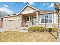 Inviting home exterior showcasing a covered porch, tan paint, brick accents, and a well-manicured lawn at 10843 W Hinsdale Dr, Littleton, CO 80127