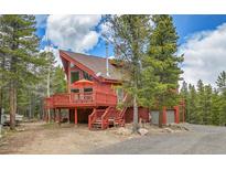 Red cabin home with a large deck nestled among the trees in a mountain setting at 387 Pine Dr, Idaho Springs, CO 80452