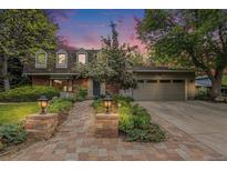Charming brick home with a manicured lawn, a brick walkway, landscape lighting, and a two-car garage at dusk at 10158 E Fair Cir, Englewood, CO 80111