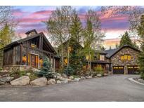 A luxurious stone and wood home with a circular driveway is framed by a vibrant sunset sky at 215 Royal Tiger Rd, Breckenridge, CO 80424