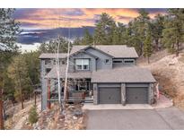 Stunning two-story gray home featuring a 2-car garage and surrounded by lush trees at sunset at 26456 Sweetbriar Trl, Evergreen, CO 80439