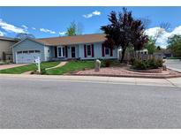 Charming single-story home with a well-manicured lawn, red accents, and mature trees creating an inviting curb appeal at 16308 E Wyoming Dr, Aurora, CO 80017