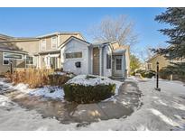 Tan two-story townhouse with a walkway and landscaping in the snow at 11565 Decatur St # 7D, Denver, CO 80234