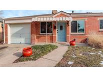 Charming brick home featuring a light blue front door, awning, garage, and attractive landscaping at 950 Jasmine St, Denver, CO 80220