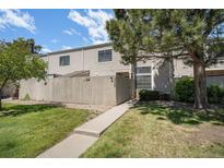 Charming townhome exterior with well-maintained lawn, trees, and concrete walkway to fenced entry at 7705 W 87Th Dr, Arvada, CO 80005