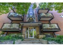 Brick apartment building featuring a glass-enclosed stairwell and balconies with green foliage in the front at 1245 Columbine St # 306, Denver, CO 80206