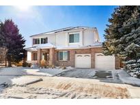 Two-story brick home with a large front yard, two-car garage, and snowy landscape at 11821 Joplin Ct, Commerce City, CO 80022