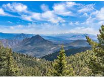 Expansive mountain vista with snow-capped peaks and evergreen forests under a blue sky with scattered clouds at 13288 Elsie Rd, Conifer, CO 80433