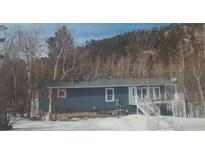 Blue home with a flat roof and stairs leading to a porch, all surrounded by trees at 629 Copperdale Ln, Golden, CO 80401