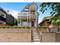 Charming two-story home with a red door, white railings, and beautiful landscaping at 2021 Eliot St, Denver, CO 80211
