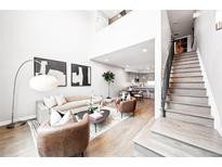 Bright living room with modern furniture, light wood floors, and access to the kitchen and staircase at 1555 W 43Rd Ave, Denver, CO 80211