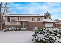 Charming two-story home featuring a brick facade and a cozy bay window, all dusted with a fresh layer of snow at 1520 Phillips Dr, Northglenn, CO 80233