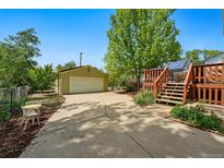 View of a backyard featuring a driveway, detached garage, and wooden deck with stairs leading up from the driveway at 5573 S Datura St, Littleton, CO 80120