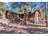 Beautiful log home with a green roof, stone accents, and mature trees on a spacious lot at 1772 E Timber Meadow Ct, Franktown, CO 80116