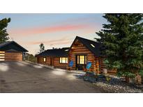 Charming log home with a black roof and two inviting blue chairs on a paved drive way at 1651 Pine Valley Rd, Evergreen, CO 80439