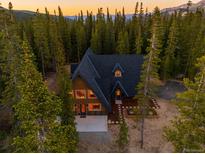 Stunning mountain home with a roof and wood-paneled A-frame exterior surrounded by lush forest at sunset at 297 Robertson Ln, Breckenridge, CO 80424