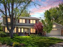 Charming two-story home with a well-manicured lawn, mature trees, and red shutters at dusk at 4175 S Sidney Ct, Denver, CO 80237