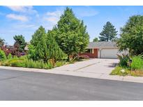 Charming single-story home with lush trees, a well-manicured lawn, and a long, wide driveway at 370 S Parfet St, Lakewood, CO 80226