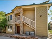 Two-story tan condo featuring a stone accent, open stairway, and clean landscaping at 9911 E Idaho Cir # 202, Denver, CO 80247