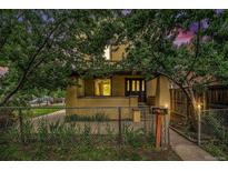Charming two-story yellow home featuring a covered porch, mature trees, and fenced front yard at 7 Elati St, Denver, CO 80223